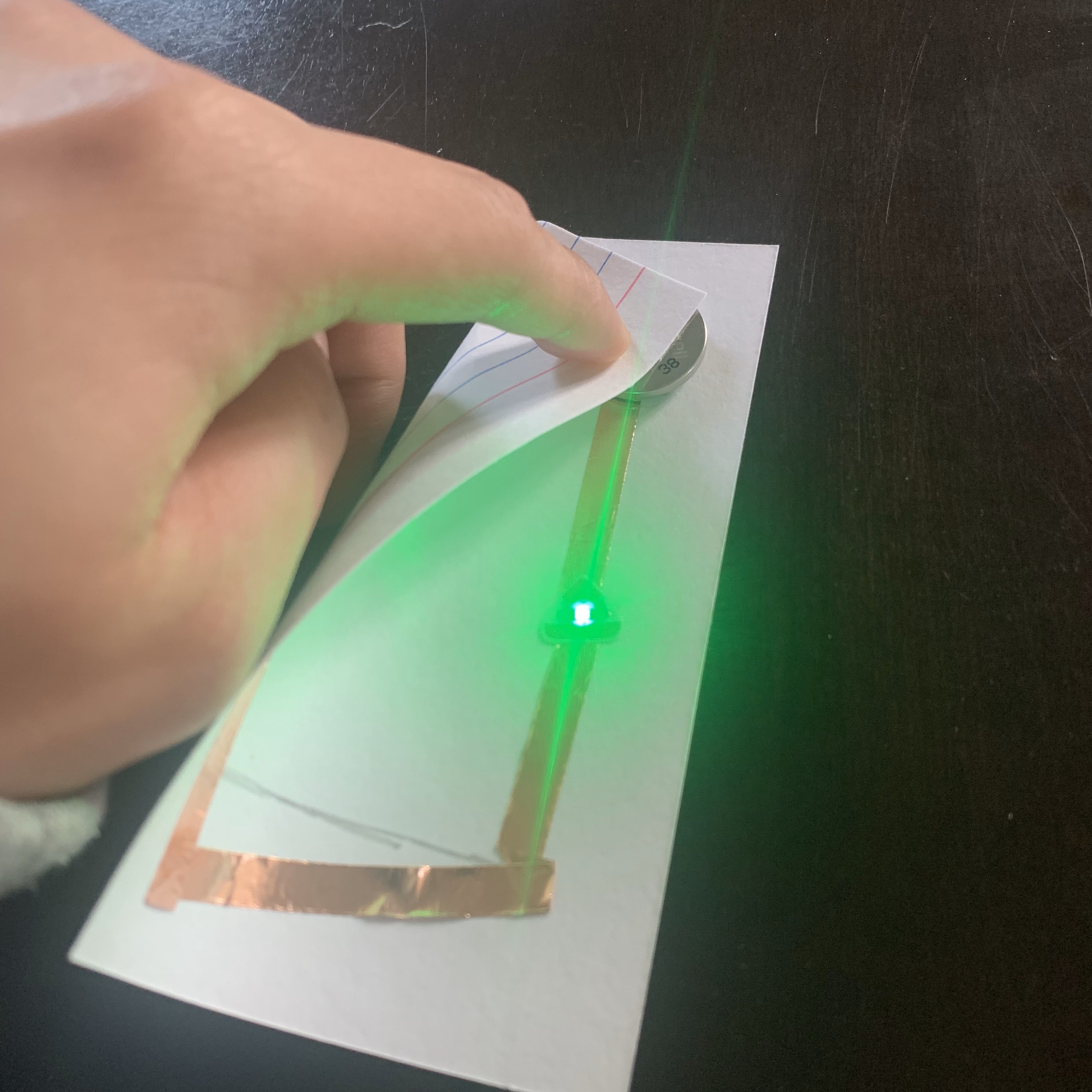 Displayed a test of the second circuit flipping the corner of the paper which had the positive endpoint. LED Light successfully lit up green.